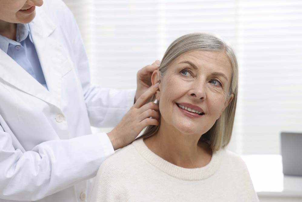 Audioprotesista poniendo audífono en el oído del paciente en la clínica, primer plano